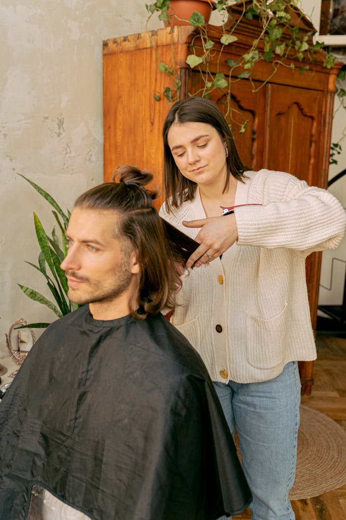 A young woman styles a mans hair indoors, in a modern salon setting.