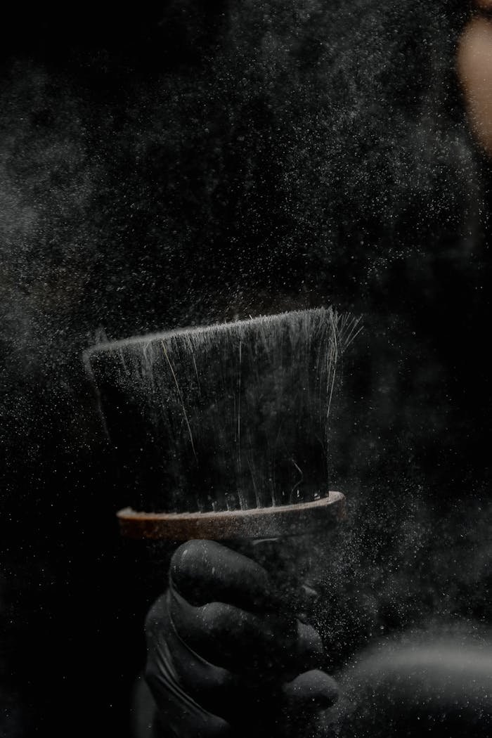 A detailed view of a barbers brush with dust particles against a dark background.